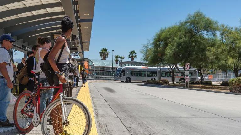 People stand under a bus shelter as a commuter bus approaches