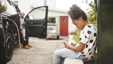 A girl sitting on a wall while an electric car is charging