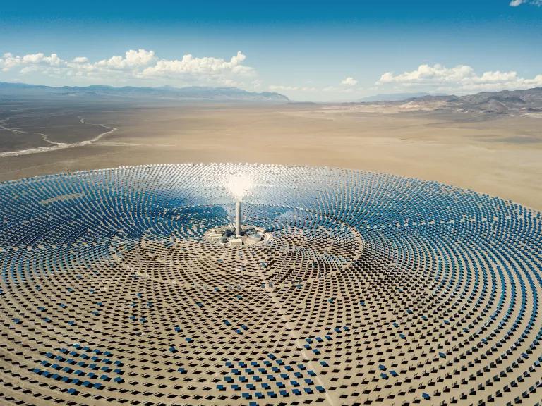 Sunlight is reflected by mirrors toward a tall receiver tower at a concentrated solar-thermal plant.